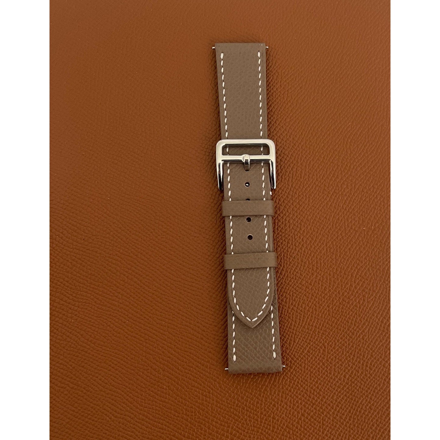 Taupe Epsom leather watch strap with white stitching and silver buckle, flat lay.
