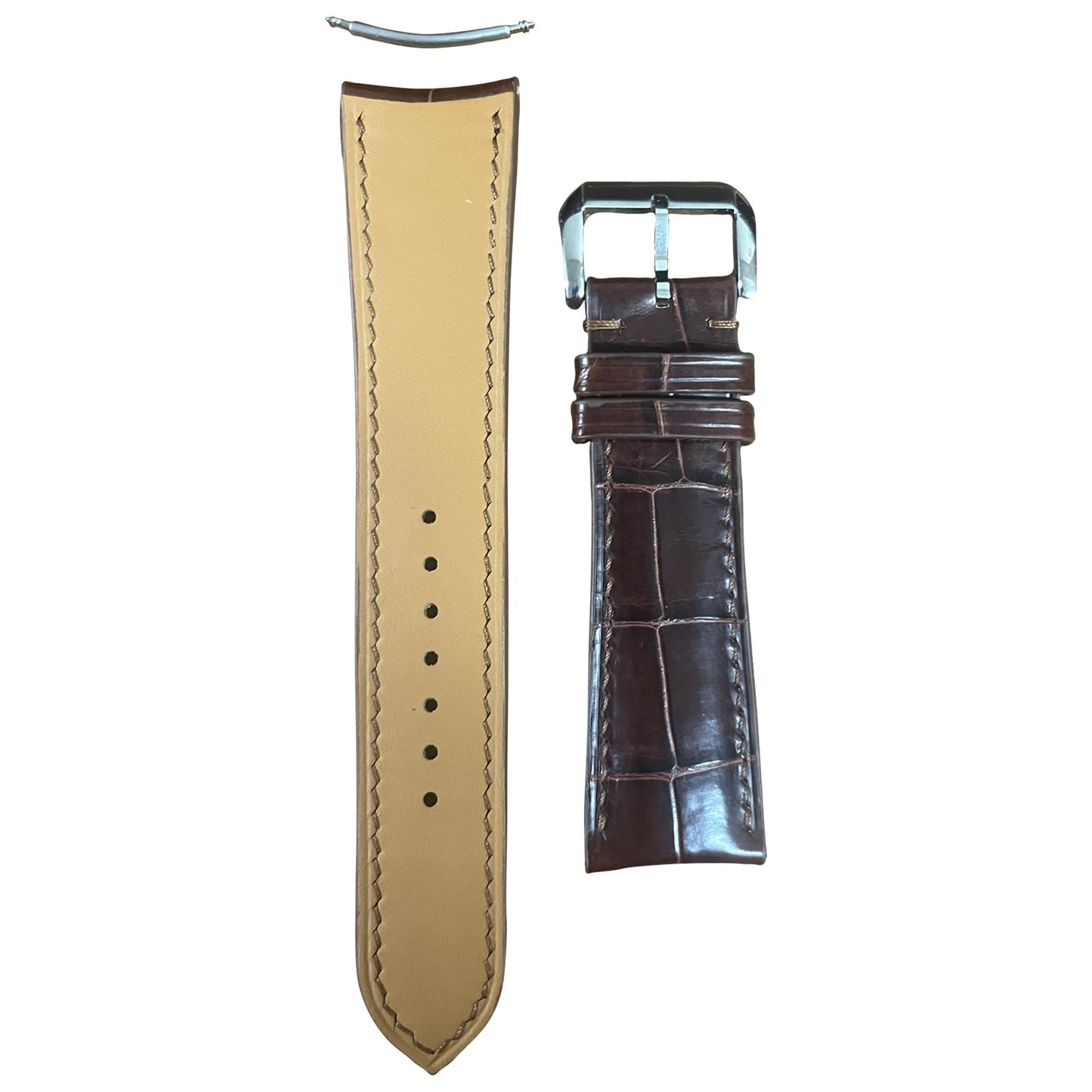 Flat lay of a brown crocodile leather watch strap with a silver buckle and tan leather lining.