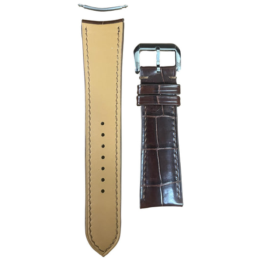 Flat lay of a brown crocodile leather watch strap with a silver buckle and tan leather lining.