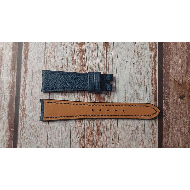 Flat lay of a blue leather watch strap with tan lining and black stitching.