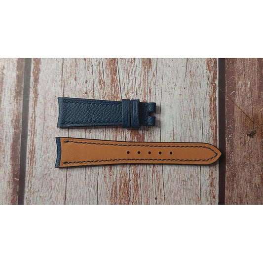 Flat lay of a blue leather watch strap with tan lining and black stitching.