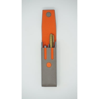 Epsom leather pen holder in grey and orange with a gold pen, flat lay.