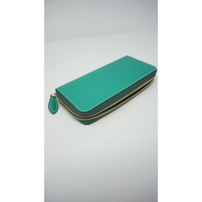 Teal Epsom leather clutch wallet with gold zipper and white stitching, angled view.