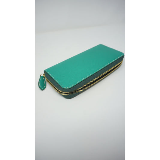 Teal Epsom leather clutch wallet with gold zipper and white stitching, angled view.