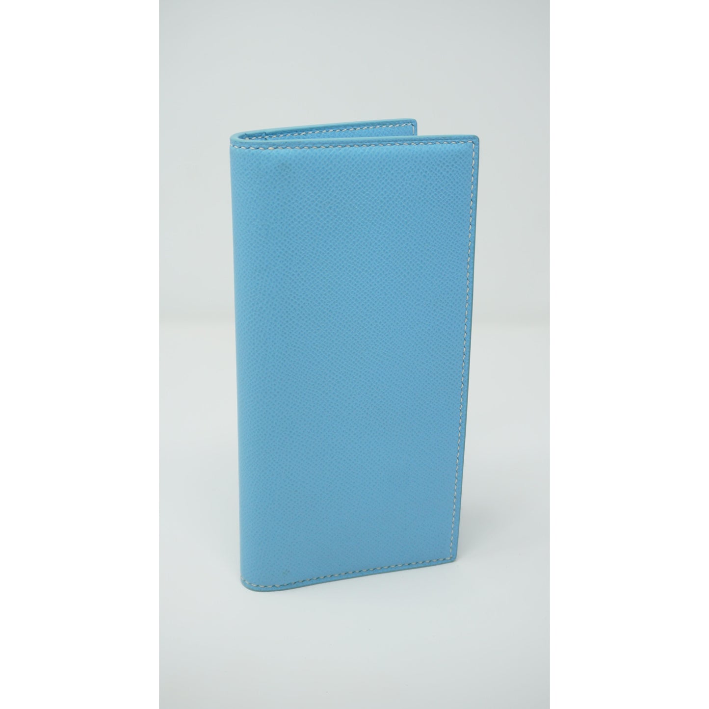 Light blue Epsom leather clutch with white stitching, standing upright.