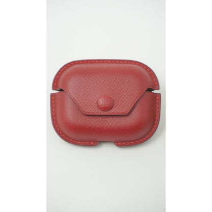 Red Epsom leather Airpods Pro case with snap closure and red stitching, flat lay.