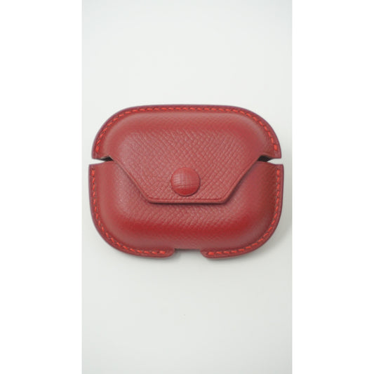 Red Epsom leather Airpods Pro case with snap closure and red stitching, flat lay.