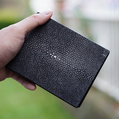 Black stingray leather wallet held in hand, showing textured surface and central pearl.