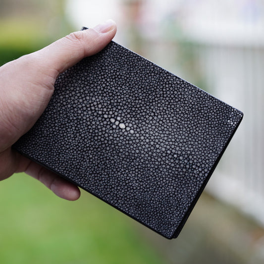 Black stingray leather wallet held in hand, showing textured surface and central pearl.