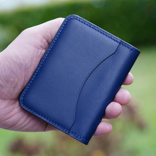 Hand holding a blue leather card holder with matching stitching and a curved front pocket.