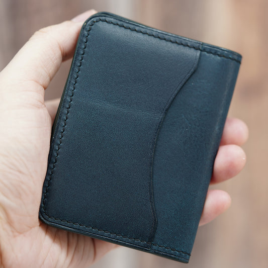 Hand holding a dark blue leather card holder with subtle texture and black stitching.