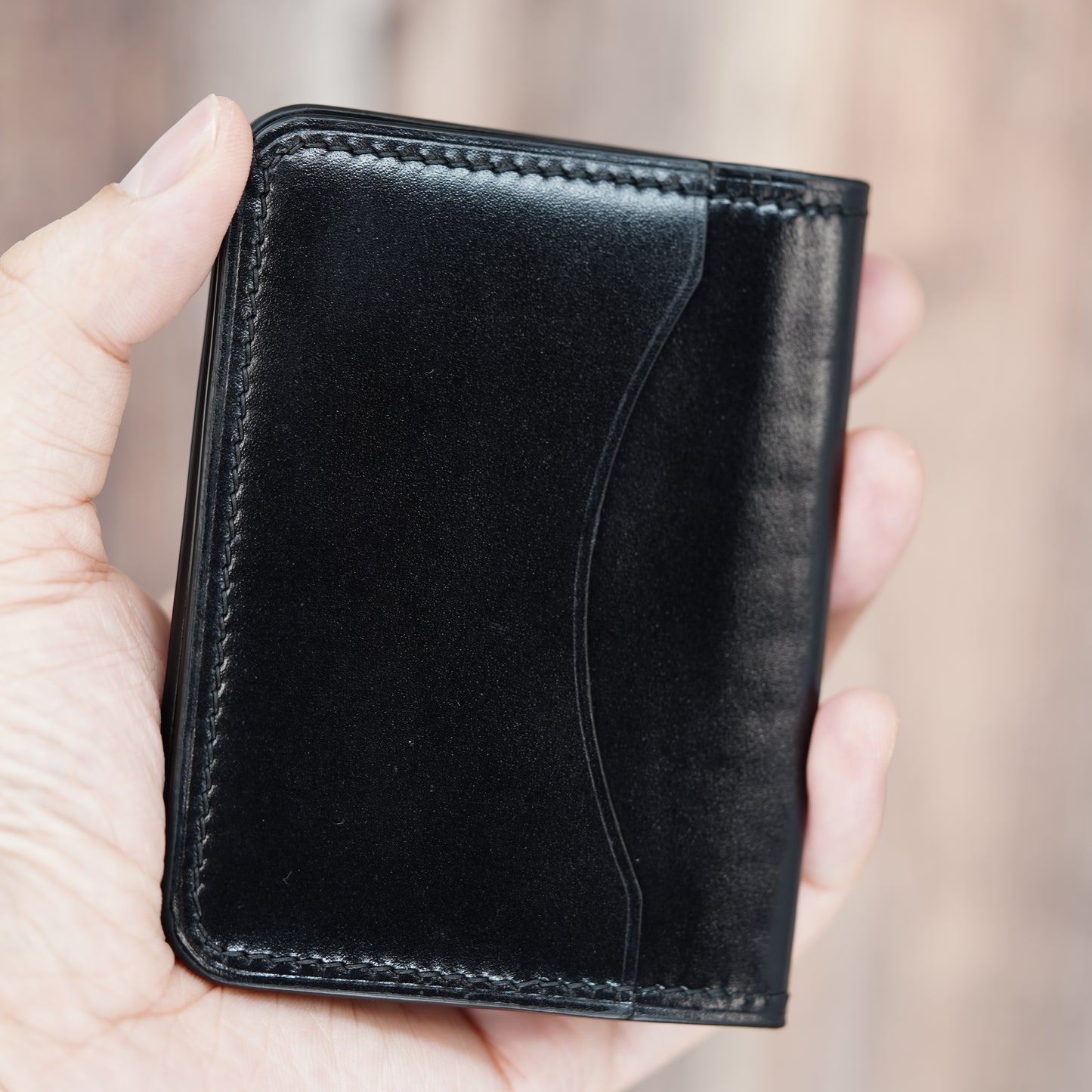 Hand holding a sleek black leather card holder with visible stitching and a curved design element.