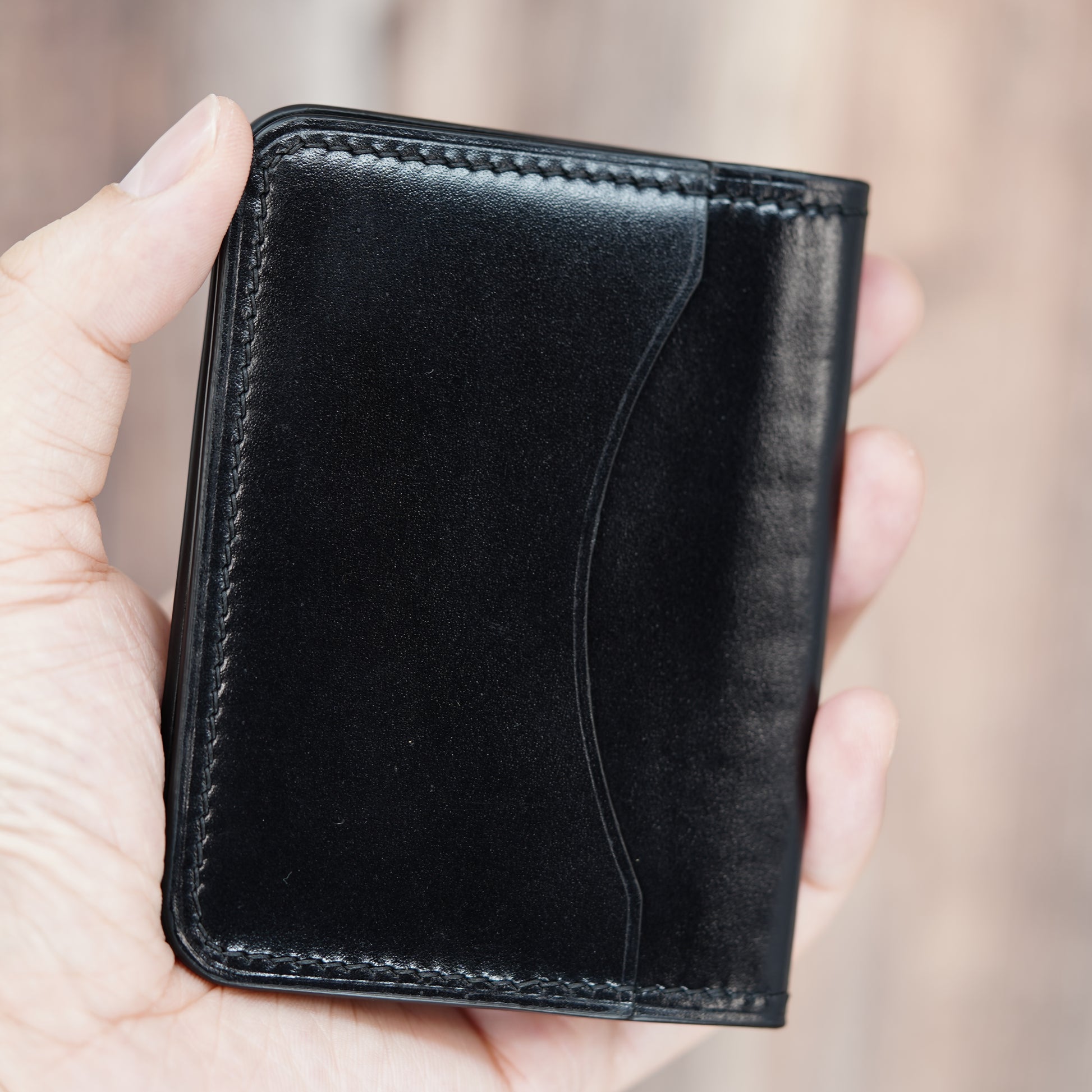 Hand holding a sleek black leather card holder with visible stitching and a curved design element.