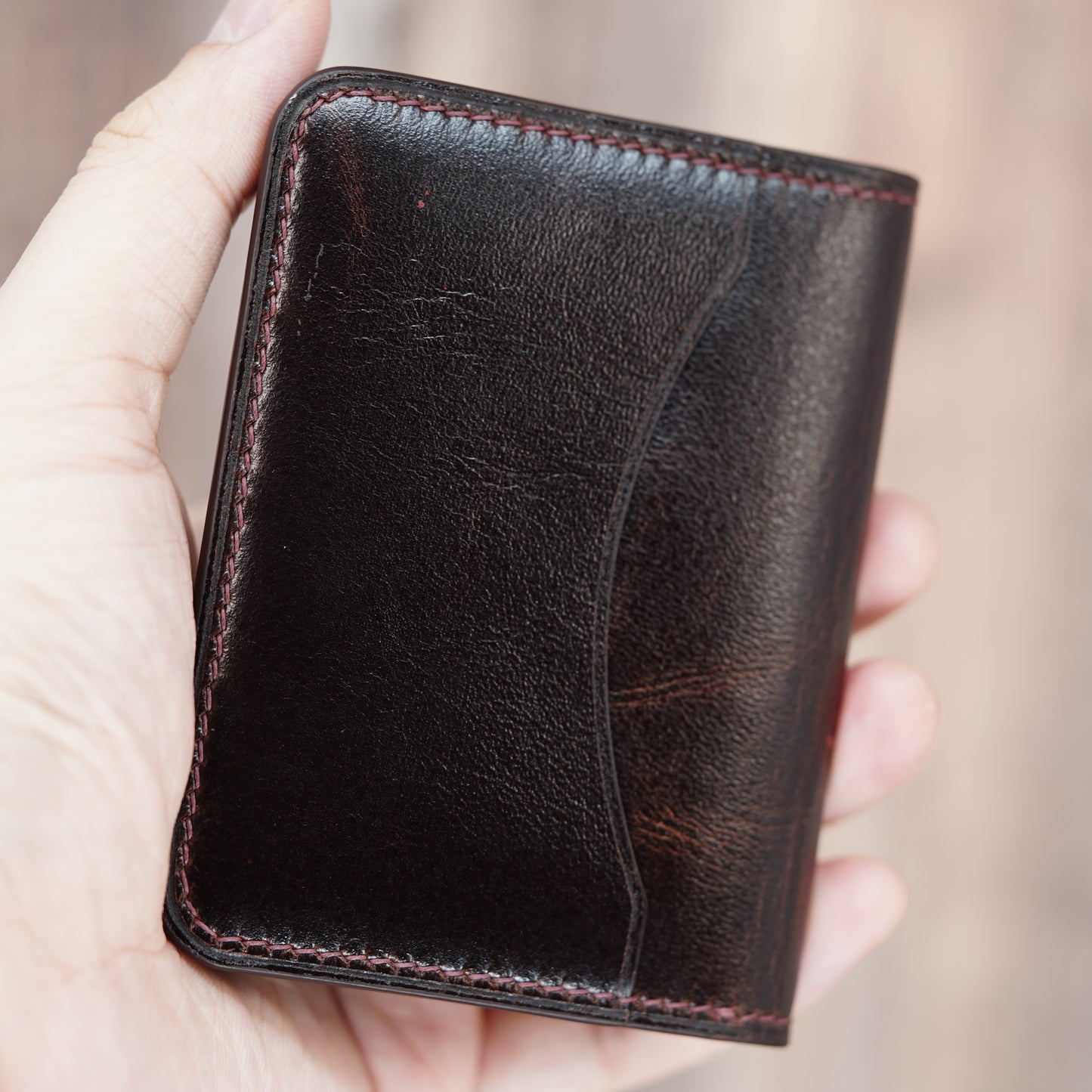Dark brown leather card holder with red stitching, held in hand.