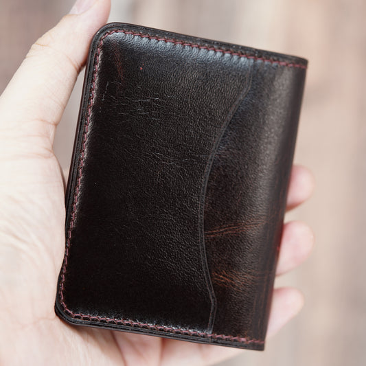 Dark brown leather card holder with red stitching, held in hand.