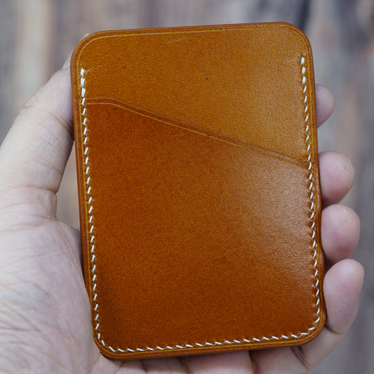 Hand holding a tan leather card holder with white stitching and two card slots.