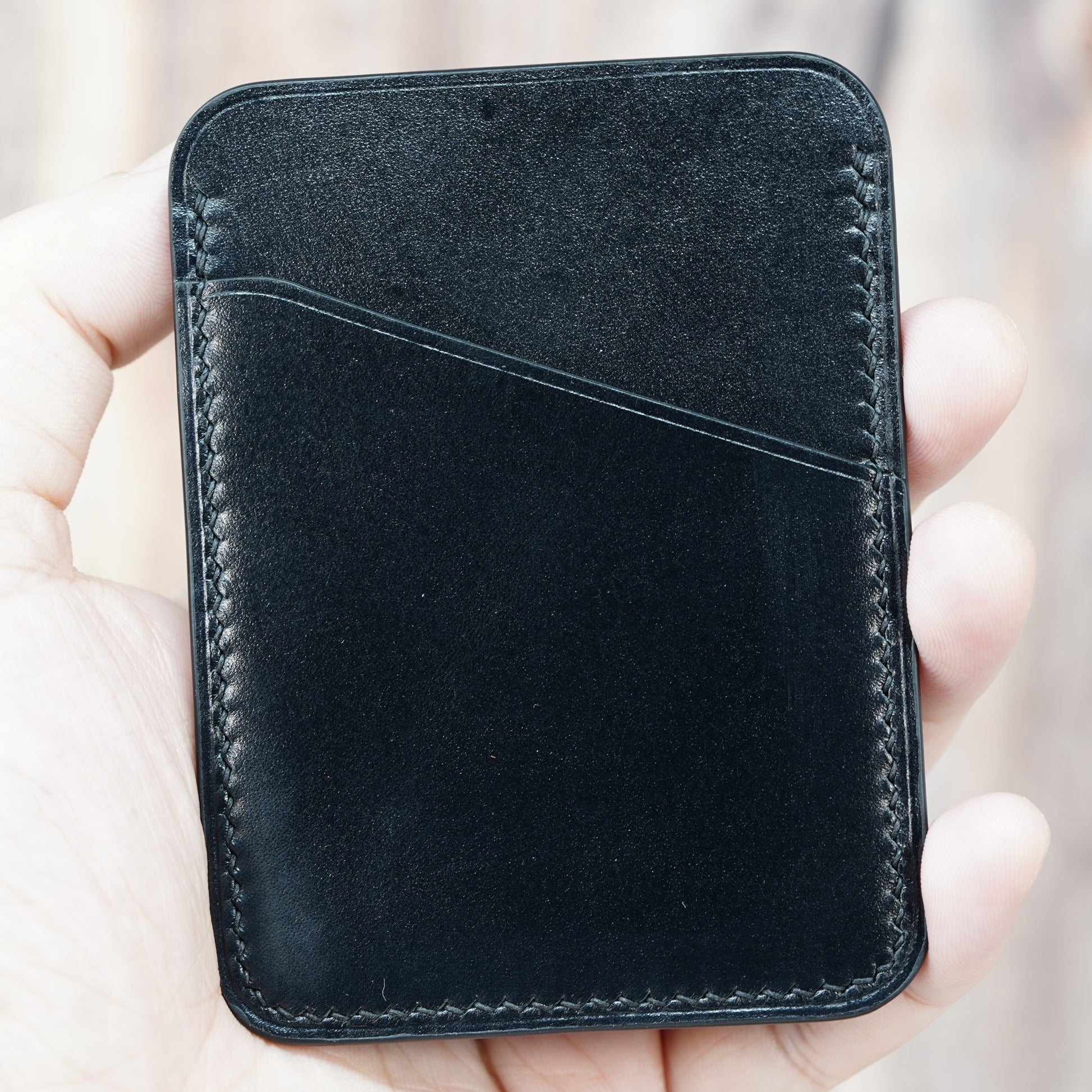 Hand holding a black minimalist leather card holder with visible stitching and a front card slot.