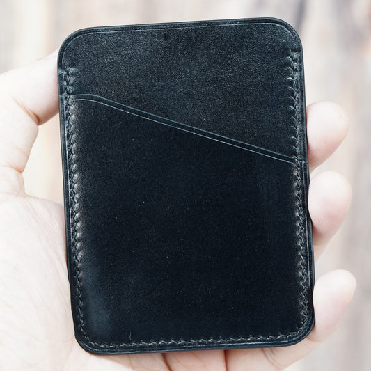 Hand holding a black minimalist leather card holder with visible stitching and a front card slot.