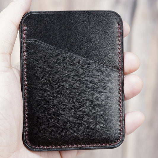 Dark brown minimalist leather card holder with red stitching, held in a hand.
