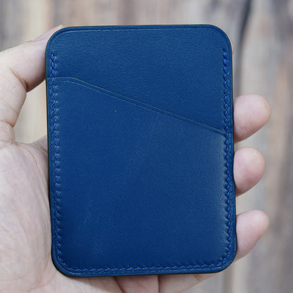 Hand holding a minimalist blue leather card holder with two pockets and blue stitching.