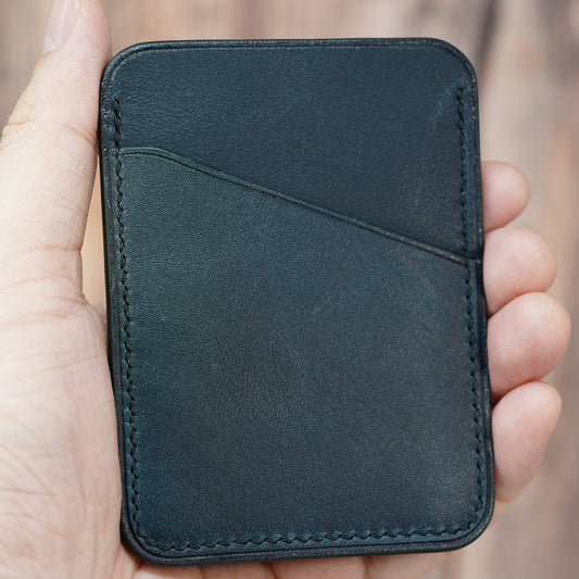 Hand holding a minimalist dark green leather card holder with diagonal pocket and visible stitching.