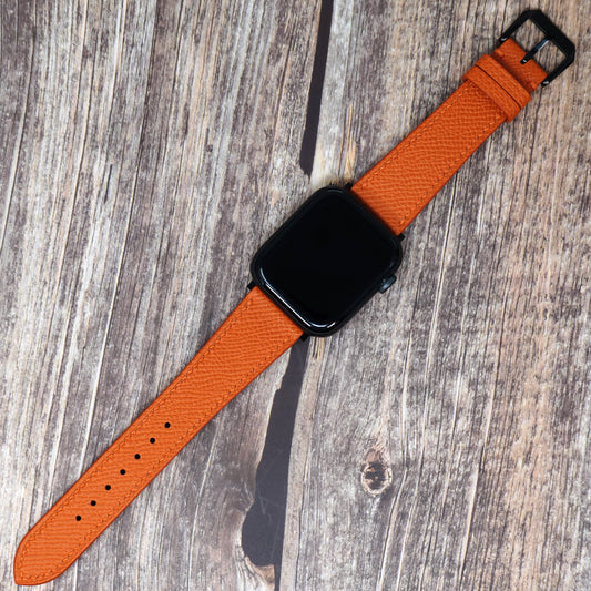 Orange Epsom leather watch strap for Apple Watch with black buckle, flat lay.