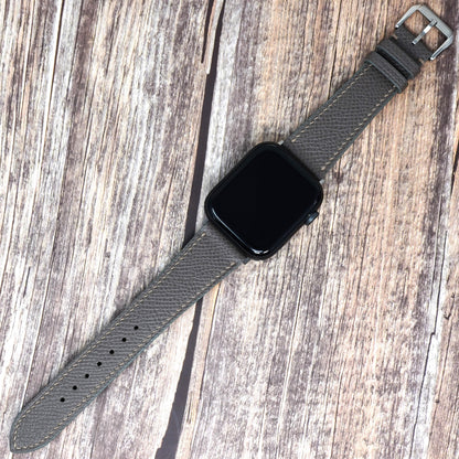 Gray Epsom leather watch strap with gray stitching and a black Apple Watch, flat lay.