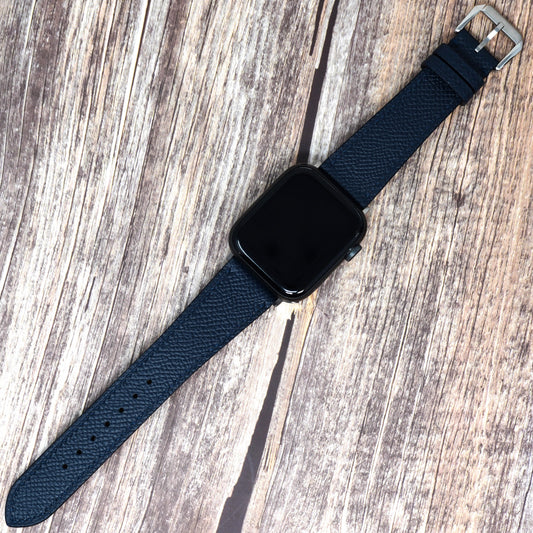 Navy Epsom leather watch strap with a black Apple Watch, flat lay on wood.
