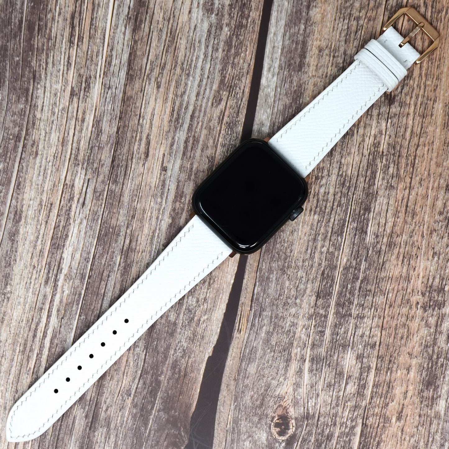 White Epsom leather watch strap for Apple Watch, with white stitching and gold buckle, flat lay.