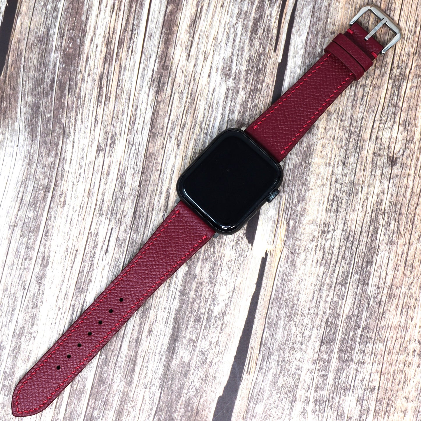 Red Epsom leather watch strap for Apple Watch, flat lay on wood.