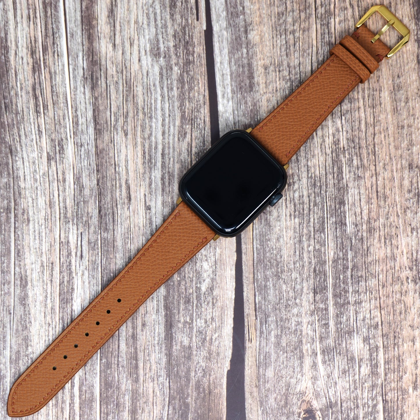 Tan Epsom leather watch strap for Apple Watch, flat lay on wood.