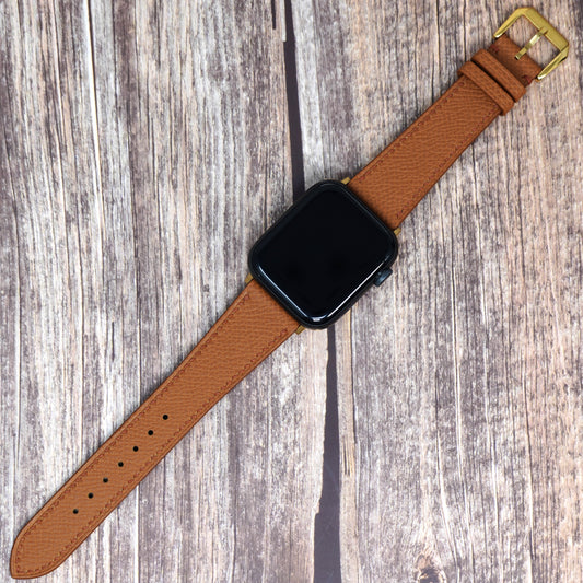 Tan Epsom leather watch strap for Apple Watch, flat lay on wood.