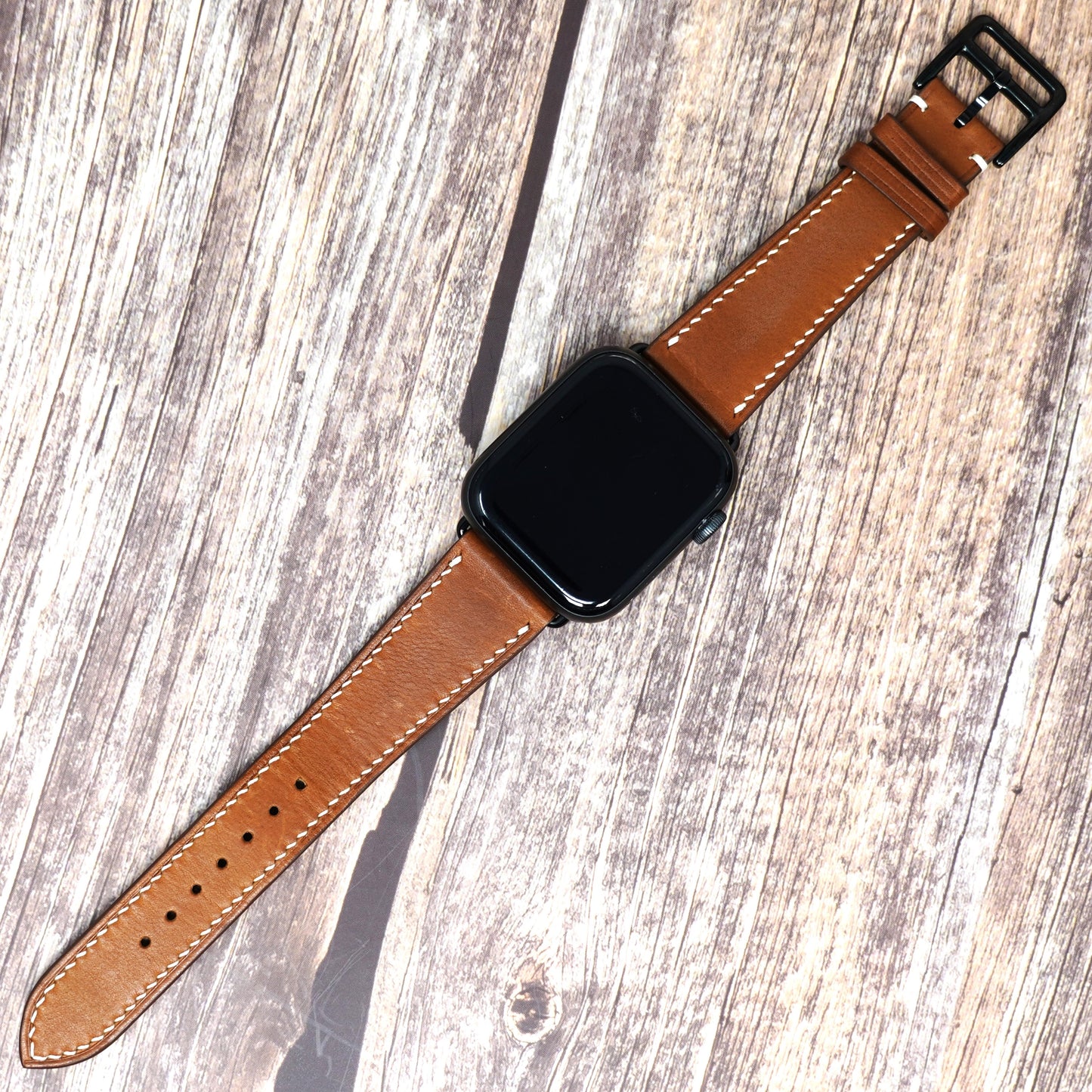 Brown Barenia leather watch strap with white stitching and black buckle, flat lay.