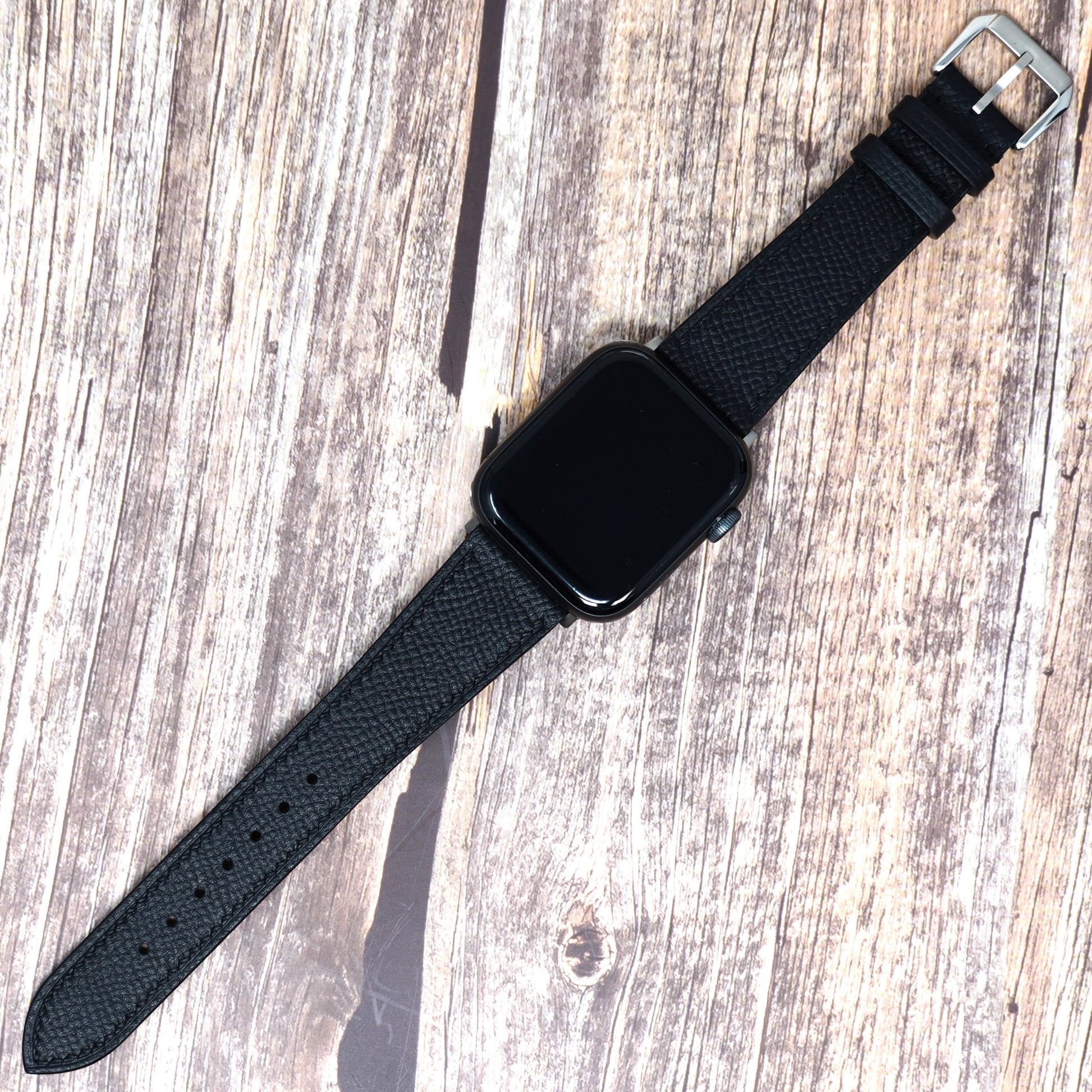 Black Epsom leather watch strap for Apple Watch with silver buckle, flat lay.