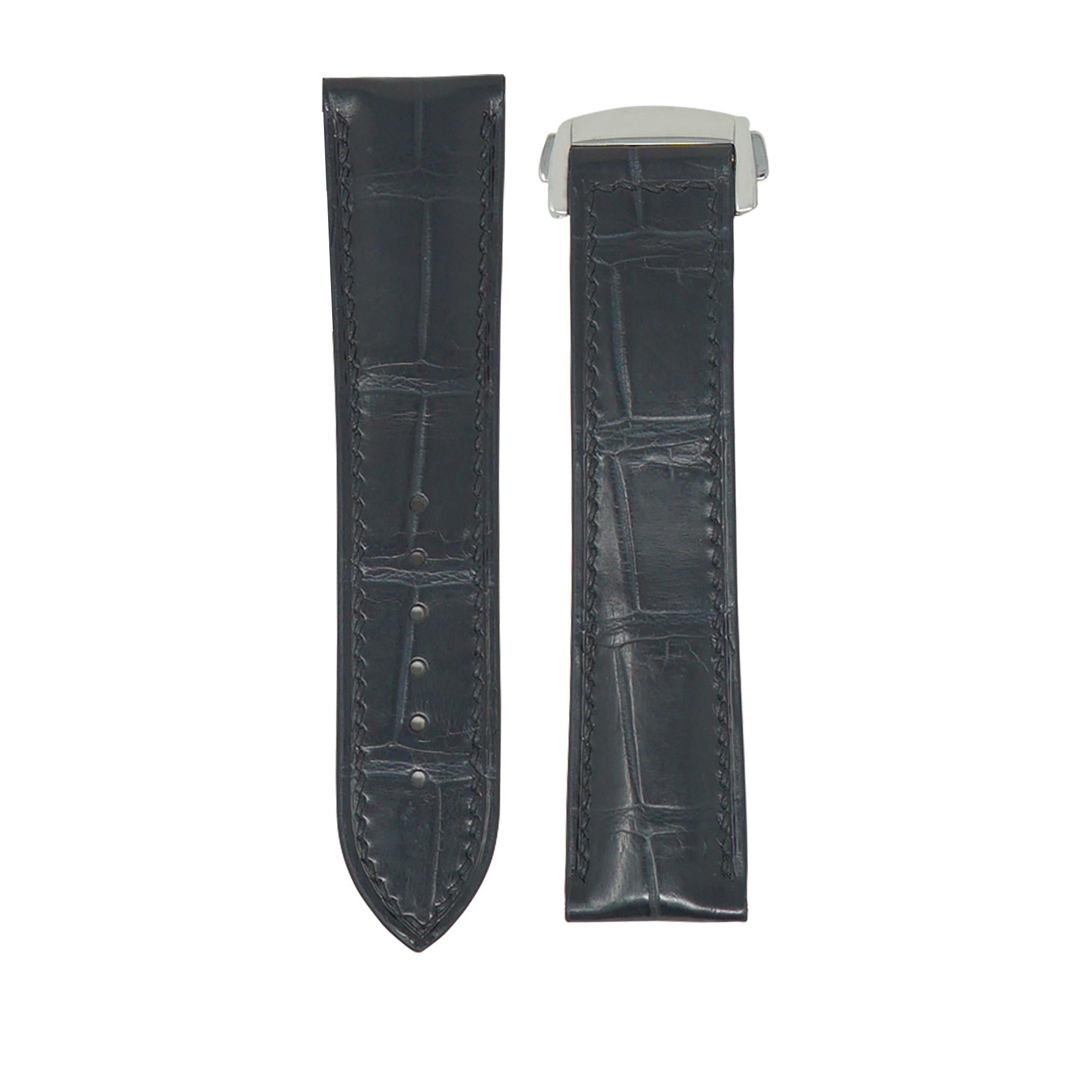 Flat lay of a dark grey crocodile leather watch strap with matching stitching and a silver deployment clasp.