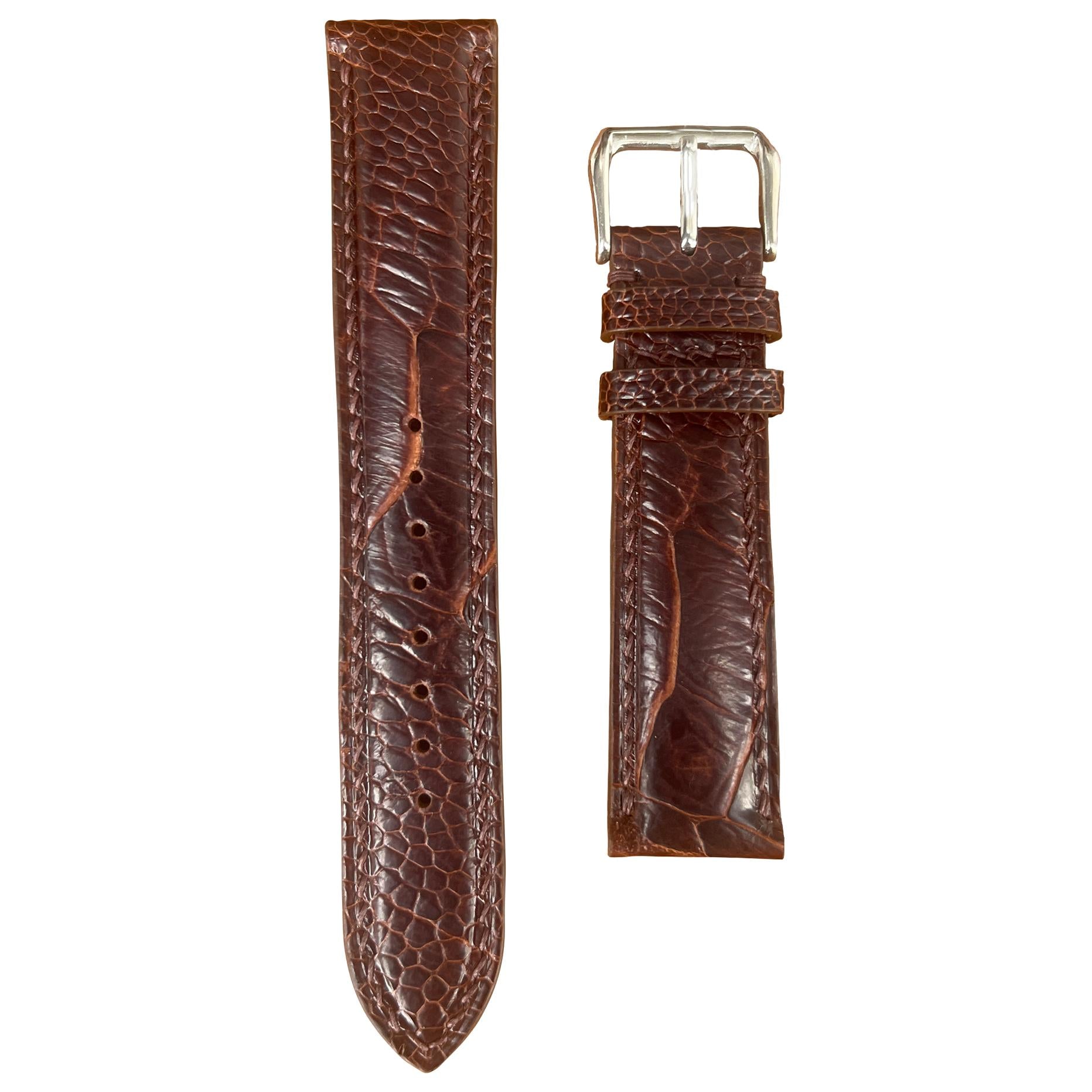 Dark brown ostrich leg leather watch strap with silver buckle, flat lay.