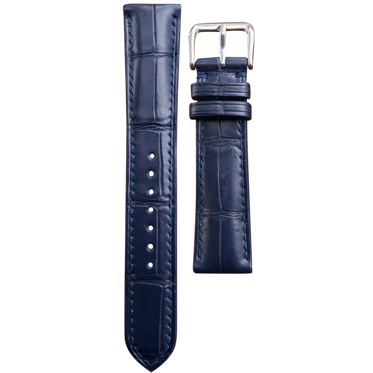 Dark blue crocodile leather watch strap with matching stitching and a silver buckle, flat lay.