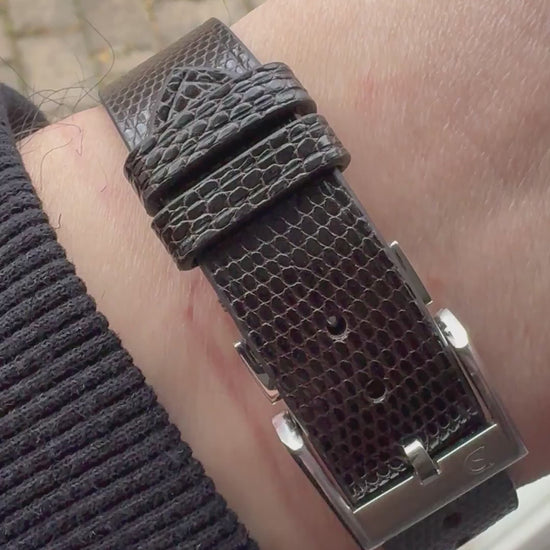 Dark brown lizard leather watch strap fitted to a steel dress watch, showing wrist fit, grain, stitching, buckle and underside.