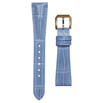 Ice blue crocodile leather watch strap with white stitching and rose gold buckle, flat lay.