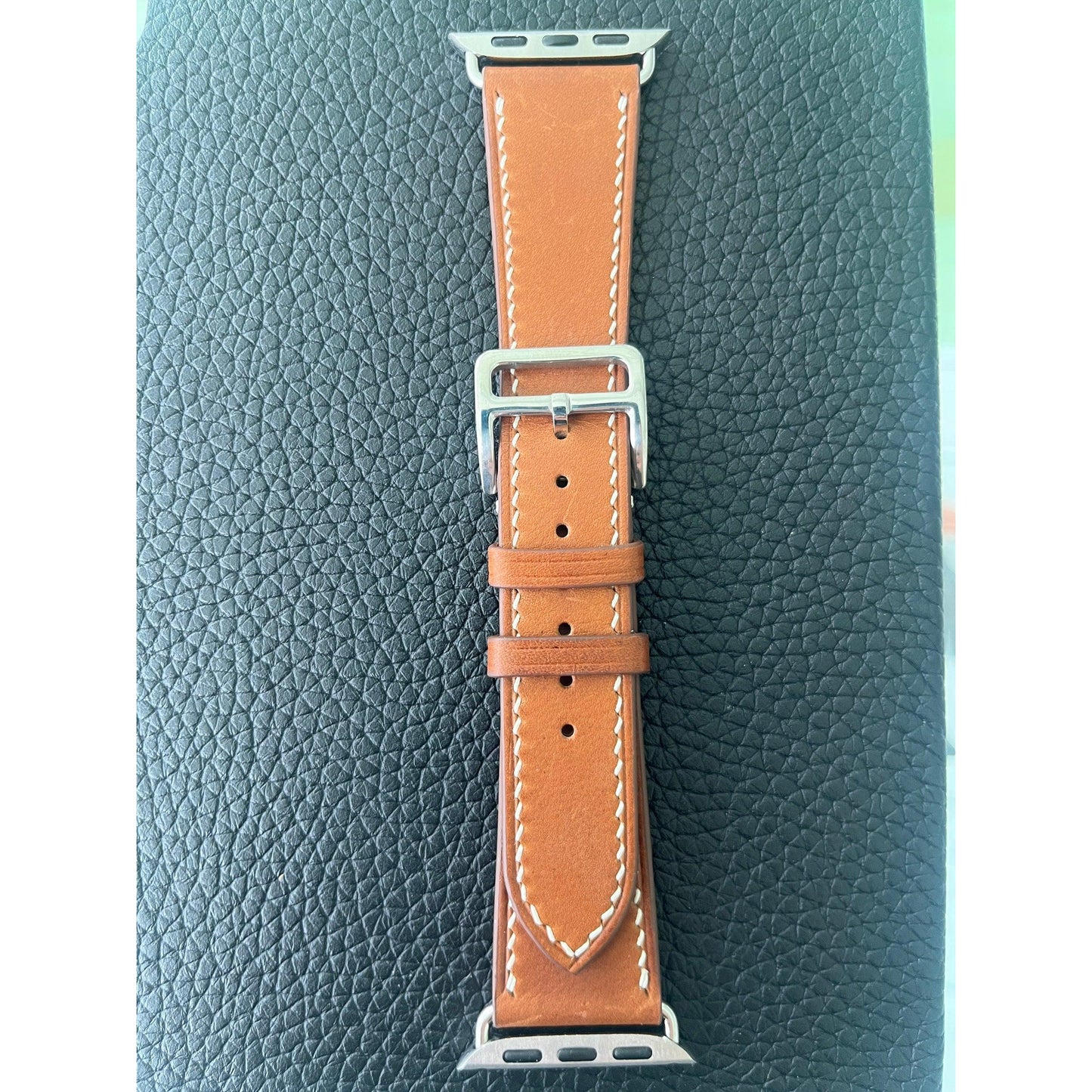 Brown Barenia leather watch strap with white stitching and silver buckle, flat lay.