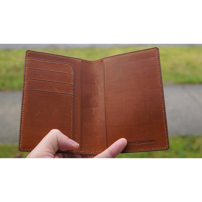 Brown Barenia leather passport holder, open view, with card slots on left and email engraved on right.